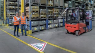 Linde TruckSpot wirft Zeichen im Lager Zwei Personen laufen im Lager und kreuzen mit einem Stapler